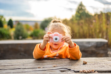Toddler Girl Taking Pictures with Pink Digital Children's Camera in the Summer Park 