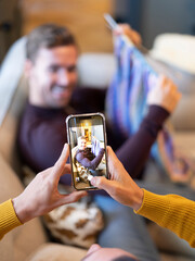 Man photographing boyfriend while knitting at home
