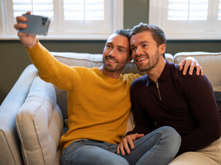 Gay couple taking selfie while sitting on sofa at home
