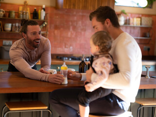 Gay couple feeding baby daughter in kitchen