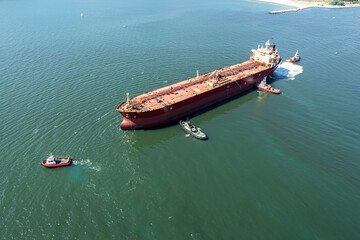 Aerial view of tug boat assisting big oil tanker. Large oil tanker ship enters the port escorted by tugboats.