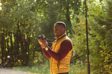 Close-up african american guy portrait photographer taking picture with photo camera on city green park copy space - leisure activity, diversity and hobby concept