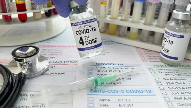Technican holding Coronavirus vaccine vial fourth dose for new variants of Sars-cov-2 virus on test requisition form. Doctor holding COVID-19 vaccine vial 4th dose for booster shot for omicron variant