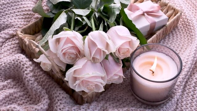 Tray with  bouquet of beautiful pink roses and gift box and burning candle on bed. 
