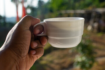 Mans hand holding tea cup on backgrounds of mountains with green plant morning in India Kerala Munnar