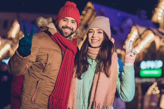 Photo of funky brunette student couple show v-sign wear hat jacket scarf on christmas fair outdoors