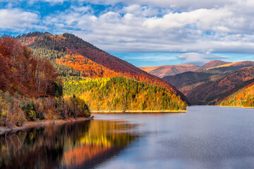 Malerischer Blick auf den herbstfarbenen Wald, der sich im warmen Oktoberlicht gegen den dramatischen Himmel zum Alpensee in den siebenbürgischen Alpen spiegelt