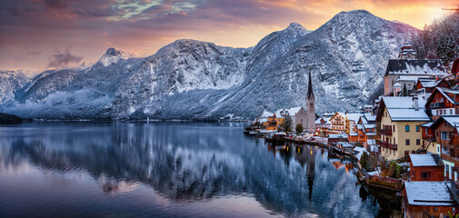 Panoramic view of the little village of Hallstatt, Austria, during winter sunset time with snow, glowing sky in the mountains and warm lights from the houses