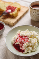 Homemade ricotta soft cheese or cottage cheese served with raspberry jam and fresh bread and cup of cocoa on linen tablecloth. Healthy cozy breakfast. Selective focus - 546896245