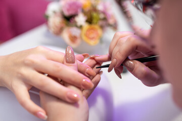 Close-up of a girl doing a manicure in a beauty salon. Nail care. Manicurist corrects the applied varnish with a thin brush. Cosmetic procedure