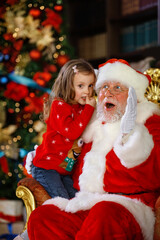 Fototapeta na wymiar Santa Claus hugs the child and promises to fulfill his cherished wish. A smiling little girl on Santa's lap.