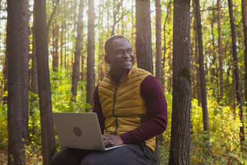 African american man sitting in city park on a bench with laptop studying online outdoors. Man freelancer learn working remotely in street e-learning