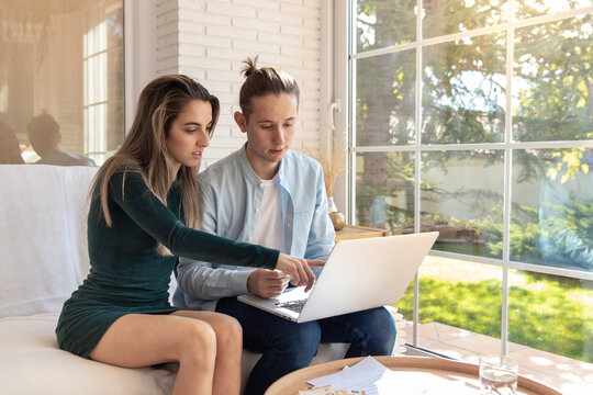 Young couple revising the financial for home budget revision concept in the laptop sitting in the sofa in the living area at home