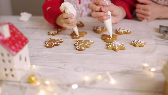 Mother and daughter prepare Christmas cookies and decorate them with icing for a happy holidays