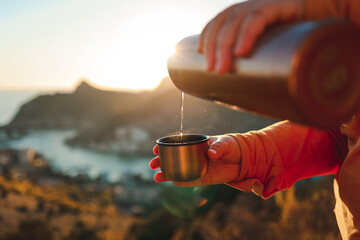 A human pours hot tea from a thermos into a mug on the mountain. Concept of autumn outdoor...
