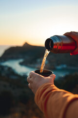 Naklejka premium A human pours hot tea from a thermos into a mug on the mountain. Concept of autumn outdoor recreation. 