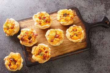 Crispy mini cups of puff pastry stuffed with eggs, cheese and ham close-up on a wooden board on the...