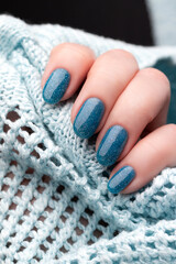 Fototapeta na wymiar Female hand in blue knitted sweater with beautiful holiday manicure - blue glitter nails. Nail care concept