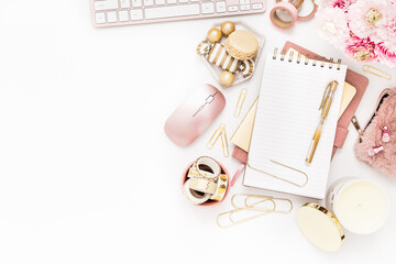 A femininely styled desktop in shades in gold and dusty pink with modem stationery. Lifestyle theme inspired by the office workspace of a stylish woman. Flat lay with fresh flowers pink keyboard and