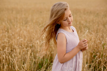 Fototapeta na wymiar a beautiful blonde girl in a pink linen dress stands in a wheat field and touches her with her hands