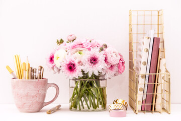 A femininely styled desktop in shades in gold and dusty pink with modem stationery. Lifestyle theme inspired by the office workspace of a stylish woman. With fresh flowers including Ranuculus