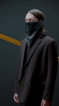 Vertical medium portrait studio portrait footage of stylish young Caucasian man wearing black outfit with leather mask standing in darkness with eyes closed