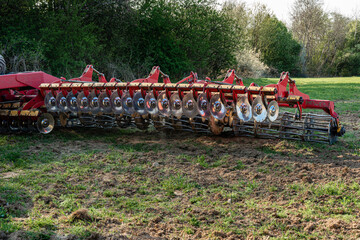 A red modern harrow stands in a field before sowing. Hydraulic mechanism for grinding the soil...