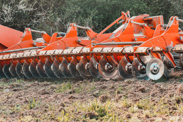 A red modern harrow stands in a field before sowing. Hydraulic mechanism for grinding the soil...