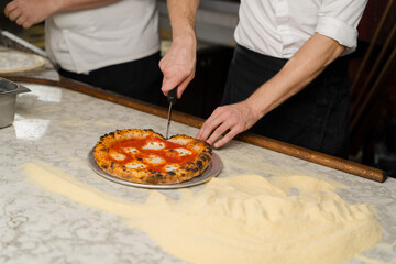 A professional chef cuts Margherita pizza with a knife in the restaurant kitchen. Traditional Italian cuisine