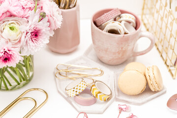 A femininely styled desktop in shades in gold and dusty pink with modem stationery. Lifestyle theme inspired by the office workspace of a stylish woman. With fresh flowers including Ranuculus