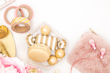 A femininely styled desktop in shades in gold and dusty pink with modem stationery. Lifestyle theme inspired by the office workspace of a stylish woman with pink earbuds, purse and sweet treats