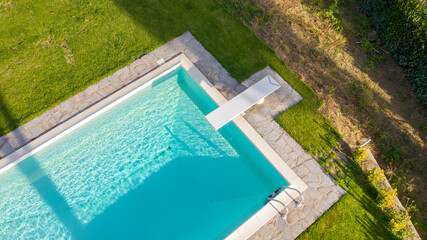 Aerial view of a rectangular swimming pool with diving board, belonging to a large villa. The water...