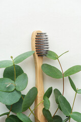 A wooden toothbrush with a sprig of eucalyptus on a gray background