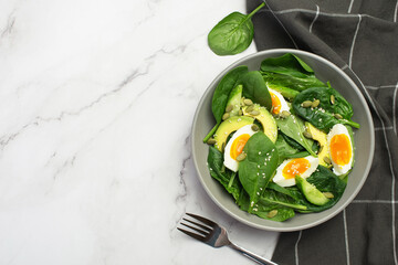 Fresh green salad with egg, avocado and spinach on a gray background in a gray plate.