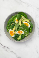 Fresh green salad with egg, avocado and spinach on a gray background in a gray plate.