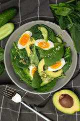 Fresh green salad with egg, avocado and spinach on a gray background in a gray plate.