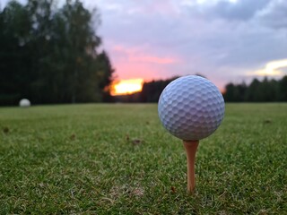 Golf ball on tee and green grass with sunset closeup