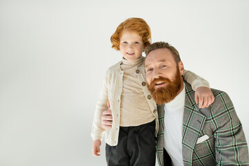 Smiling bearded father hugging redhead son isolated on grey