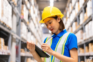 Beautiful asian woman engineer wearing safety helmet and reflective vest, She checking goods and supplies on shelves with tablet in ware house. Logistic and business export concept.