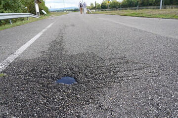 Asphalt road with a small pothole full of rainwater in low angle view. Road around the pothole is...