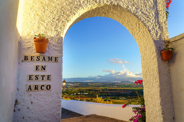 Whitewashed wall arch in an old village of Andalucia with a sign for couples to kiss.