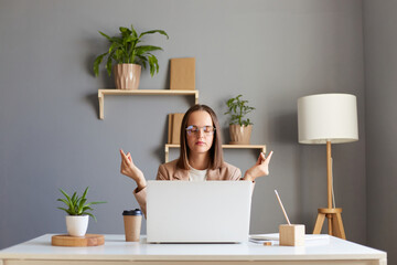 Calm businesswoman taking break for meditation, doing yoga exercise at workplace, mindful...
