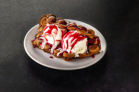 Hong Kong chocolate bubble waffle with ice cream and strawberry or raspberry syrup on dark background with copy space.