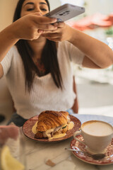 Chica joven guapa morena desayunando croissant relleno en cafeteria estilo cozy