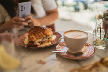 Chica joven guapa morena desayunando croissant relleno en cafeteria estilo cozy