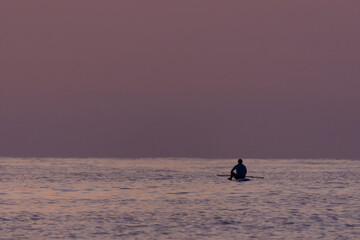 Naklejka premium Unrecognizable man sitting on a paddle board in the sea while appreciating the sunrise