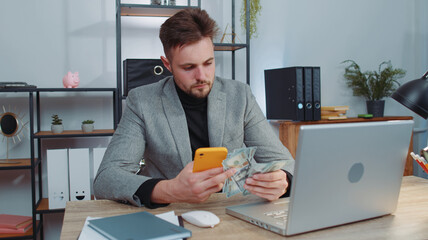 Rich businessman in suit working on smartphone counting money cash, calculate earnings income profit at office workplace. Professional manager freelancer man. Business people. Employment, occupation