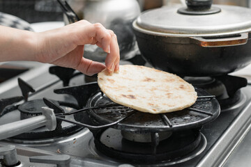 detailed view, from the hand of a girl grilling an arepa on the grill, turning it over so it...