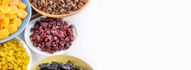 Food banner with dried apricots, cranberries, raisins, and prunes on plates on a white background with copy space. Healthy snack - mix of organic dry fruits. Vegan and vegetarian products. Banner size