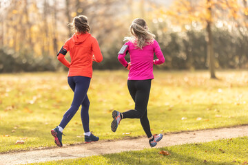 Two young fitness women running in the autumn park